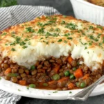 Lentil Shepherd’s Pie topped with golden mashed potatoes and fresh parsley on a white plate.