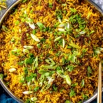 Mujadara (Lentils and Rice) garnished with scallions, cilantro, and caramelized onions in a large pot.