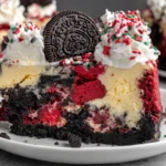 Slice of Christmas Red Velvet Cheesecake with Oreo crust, creamy vanilla cheesecake filling, red velvet chunks, whipped cream, and festive red-and-green sprinkles.