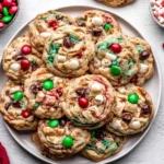 Christmas Kitchen Sink Cookies piled on a plate with colorful holiday mix-ins like M&Ms, white chocolate, pretzels, and chips.