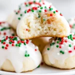 Soft Italian Christmas Cookies topped with white icing and colorful holiday sprinkles, with one cookie showing a tender, fluffy interior.
