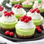 Festive Grinch Mini Cheesecakes with whipped cream and red candy topping on a black plate for a bright Christmas dessert.