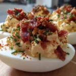 Close-up of Million Dollar Bacon Deviled Eggs topped with crispy bacon, smoked paprika, and fresh chives.