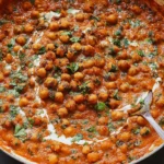One Pan Harissa Chickpeas simmered in a creamy, spicy tomato sauce with coconut milk, garnished with fresh herbs in a skillet