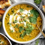 Creamy Curry Lentil Soup topped with coconut cream and fresh cilantro, served with toasted bread and lime wedges