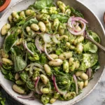 Marinated Cilantro Lime Bean Salad served in a bowl with leafy greens, white beans, red onion, and fresh cilantro lime dressing