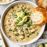 Creamy White Bean Enchilada Soup topped with avocado slices and fresh herbs, served with crusty bread