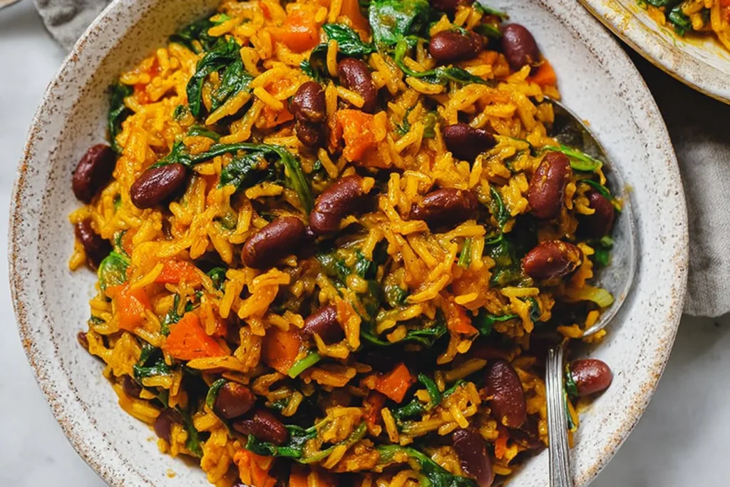 Vegan Caribbean Pelau with Beans and Spinach in a bowl—golden coconut rice with red beans, carrots, and wilted spinach.