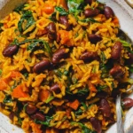 Vegan Caribbean Pelau with Beans and Spinach in a bowl—golden coconut rice with red beans, carrots, and wilted spinach.