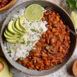 Vegan Chili Recipe served with fluffy white rice, sliced avocado, and lime wedges in a bowl, topped with fresh cilantro.