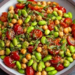 Chickpea Edamame Salad with Ginger Sesame Vinaigrette in a bowl with cherry tomatoes, sesame seeds, and sliced green onions.
