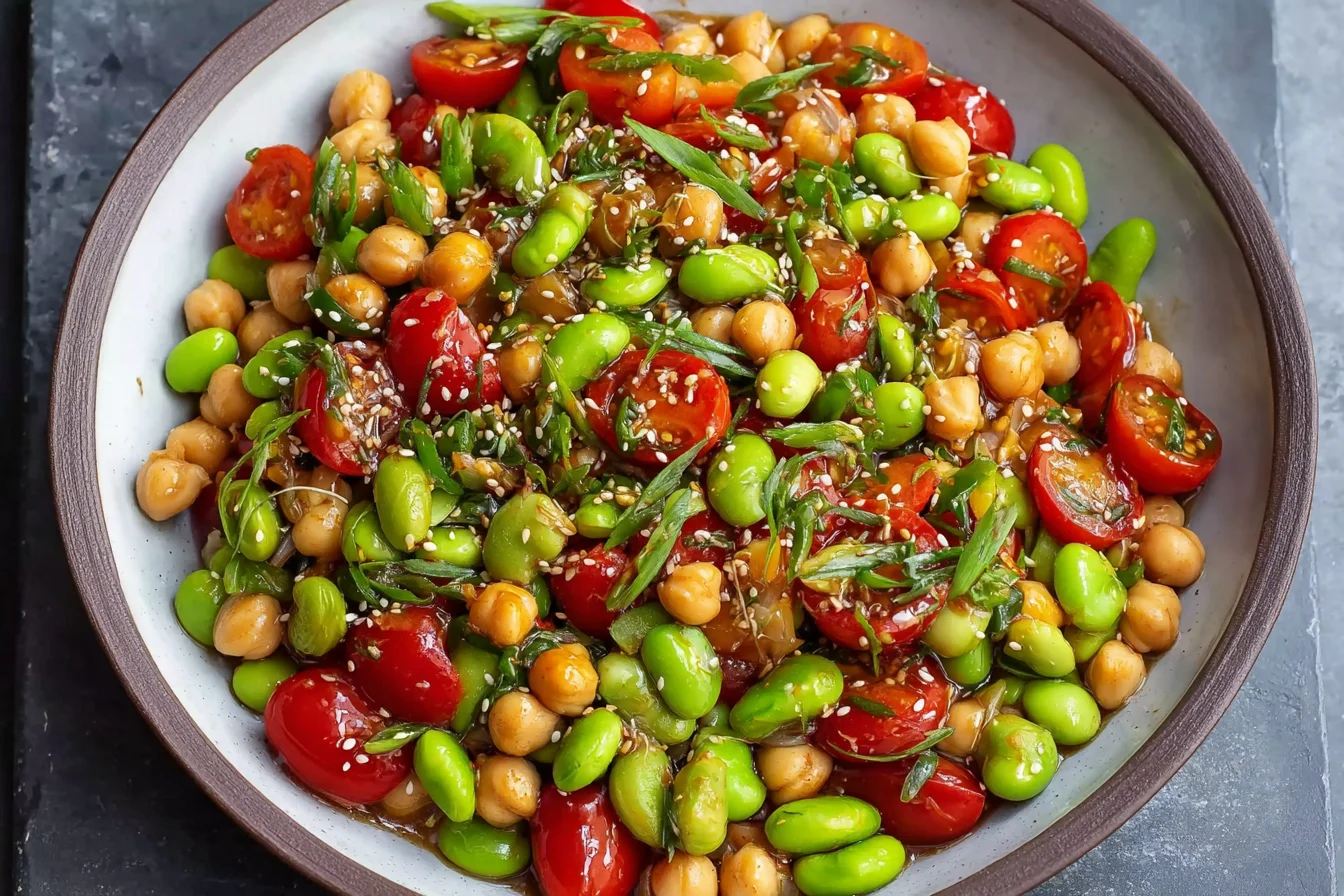Chickpea Edamame Salad with Ginger Sesame Vinaigrette in a bowl with cherry tomatoes, sesame seeds, and sliced green onions.