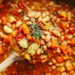 Spoonful of hearty Bean Stew with white beans, diced carrots, potatoes, tomatoes, and herbs in a rich broth.