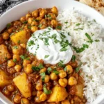Chickpea and Potato Curry served with fluffy basmati rice, topped with a dollop of yogurt and fresh herbs in a white bowl.