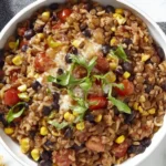 Southwest Lentils And Rice Skillet served in a white bowl with black beans, corn, tomatoes, melted cheddar, and cilantro, with lime wedges nearby.