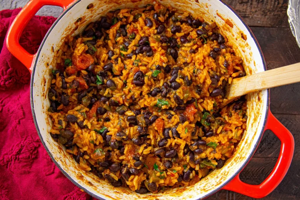 Spoon stirring one-pot Black Beans and Rice in a red Dutch oven with tomatoes, peppers, and spices.