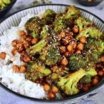 Garlic Broccoli Stir Fry With Chickpeas served over fluffy white rice, topped with sesame seeds and coated in a glossy savory sauce.