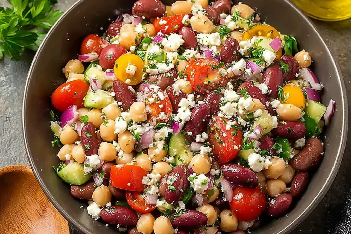 Bowl of Mediterranean Bean Salad With Feta with chickpeas, kidney beans, cucumber, cherry tomatoes, red onion, herbs, and crumbled feta.