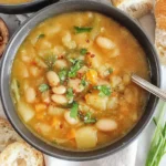 Cozy bowl of Potato and Bean Soup with cannellini beans, tender potatoes, carrots, parsley, and chili flakes served with crusty bread.