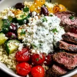 Mediterranean Steak Bowl Recipe with sliced sirloin, quinoa, cucumbers, cherry tomatoes, olives, feta, and creamy tzatziki sauce in a bowl.