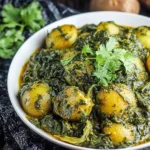 Aloo Palak (Potato and Spinach Curry) garnished with fresh herbs in a white bowl