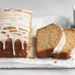 Apple Spice Cake loaf drizzled with vanilla glaze, sliced to show moist crumb, served on parchment with a cup of coffee.