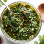 Best Ever Chimichurri Recipe in a glass jar with fresh parsley, garlic, olive oil, and red pepper flakes