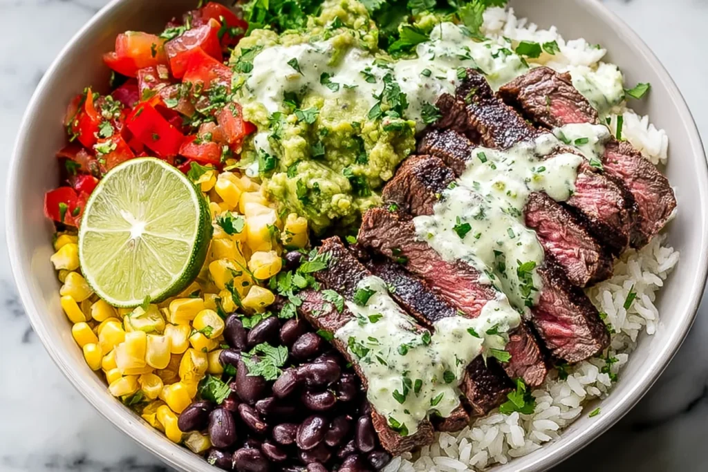 Cilantro Lime Steak Bowls with sliced steak, cilantro-lime crema, white rice, black beans, charred corn, pico de gallo, guacamole, and a lime wedge.