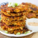 Vegetable Potato Fritters stacked on a plate with creamy sriracha mayo dip and green onion garnish