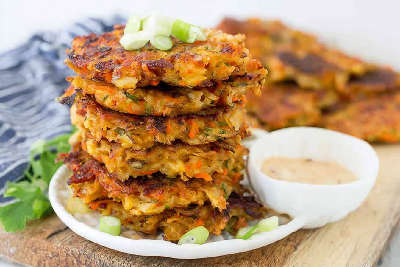 Vegetable Potato Fritters stacked on a plate with creamy sriracha mayo dip and green onion garnish