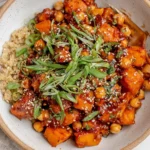 Gochujang Potatoes and Chickpeas over quinoa in a bowl, topped with scallions, parsley, and sesame seeds