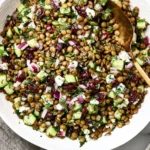 Lentil Salad with diced cucumber, red onion, herbs, and tangy lemon vinaigrette in a white bowl, topped with creamy cheese crumbles.