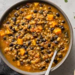 Overhead bowl of Protein Packed Black Bean and Lentil Soup with black beans, lentils, carrots, and tomato-spiced broth on a gray surface.