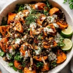 Roasted Sweet Potato Salad with Lentils in a bowl with roasted garlic tahini dressing, fresh herbs, crunchy seeds, and lime wedges