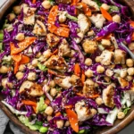 Sesame Chicken and Chickpea Salad in a wooden bowl with shredded red cabbage, carrots, chickpeas, sesame seeds, and sliced chicken with sesame dressing.