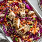 Sesame Chicken and Chickpea Salad meal prep in a glass container with diced chicken, chickpeas, red cabbage, carrots, edamame, and sesame seeds.