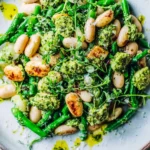 Quick & Healthy Warm White Bean Salad with arugula pesto, green beans, toasted almonds, and fresh herbs in a shallow bowl.