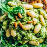 Quick & Healthy Warm White Bean Salad piled on arugula with arugula pesto, white beans, toasted pine nuts, and a drizzle of olive oil.