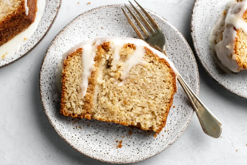 Slice of Apple Spice Cake topped with vanilla glaze on a speckled plate with a fork, showing moist and tender crumb.