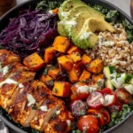 Healthy Blackened Chicken and Sweet Potato Bowls with quinoa, avocado slices, red cabbage, and greens