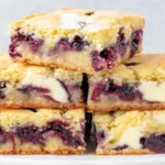Blueberry Blondies stacked on a plate with juicy blueberries and creamy white chocolate chips