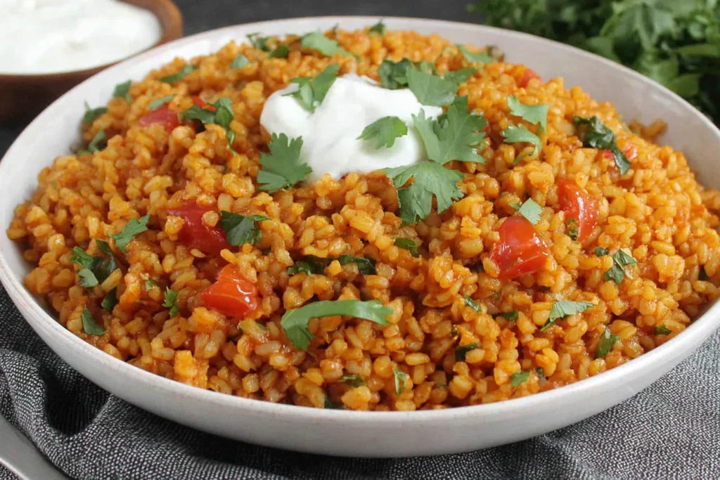 Bowl of Bulgur Tomato Pilaf topped with yogurt and fresh herbs