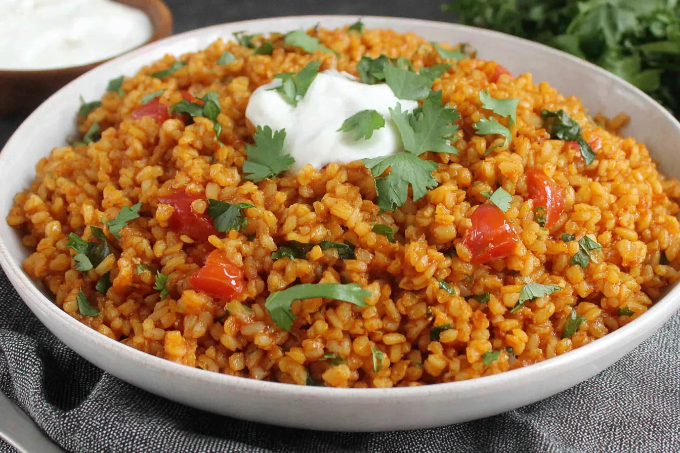 Bowl of Bulgur Tomato Pilaf topped with yogurt and fresh herbs