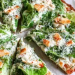 Sliced Chicken Crust Caesar Salad Pizza with romaine lettuce, parmesan cheese, croutons, and creamy Caesar dressing on a baked chicken crust