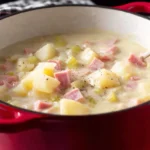 Easy and Comforting Ham and Potato Soup simmering in a red Dutch oven with diced ham and tender potatoes