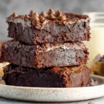 Stacked Greek Yogurt Brownies with chocolate chips and glossy ganache on a plate