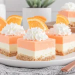 Orange Creamsicle Dream Bars squares topped with whipped cream and orange slices on a serving plate