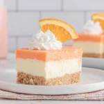 Orange Creamsicle Dream Bars slice with creamy cheesecake layer, orange topping, and Nilla wafer crust on a white plate