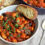 Bowl of Puttanesca Butterbeans with tomato sauce, olives, capers, and fresh parsley served with crusty bread