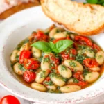 Bowl of Vegan Butter Beans with tomato and pesto, topped with fresh basil and served with toasted bread.